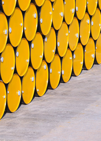 Rows of many yellow 200 liter oil drums stacked on industrial yard area in perspective side view and vertical frameの写真素材