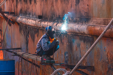 Welder on platform using arc welding machine to repairing the old rusty vessel hull at Shipyard area in evening timeの写真素材
