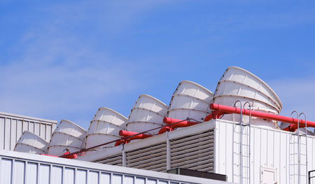 Row of white ventilation chimneys with pipelines and exhausting machine system on rooftop of factory building against blue sky backgroundの写真素材