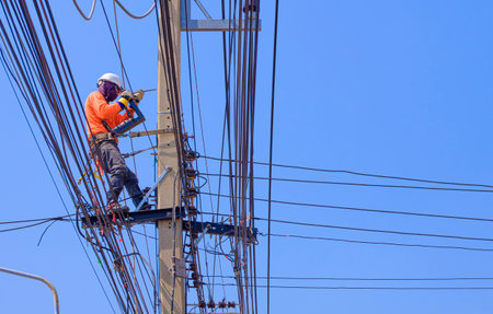 Electrician is working to install electrical system on electric power pole against blue clear sky backgroundの写真素材