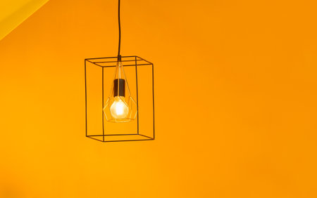Modern Golden steel cage hanging lamp glowing on yellow wall backgroundの写真素材