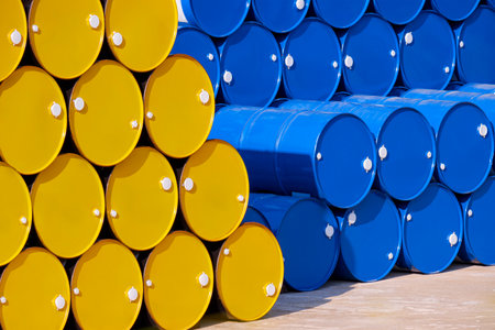 Stack of many yellow and blue 200 liter oil drums on the floor in industrial yard areaの写真素材