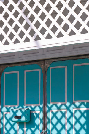 Sunlight and shadow pattern of white wooden sun shade fin on blue folding door surface of vintage house in vertical frameの写真素材