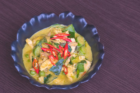 Chicken green curry in black ceramic dish on wooden table top, Thai street food styleの写真素材