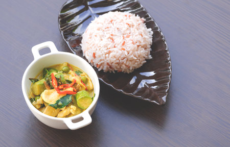Chicken green curry with steamed rice in ceramic dish on wooden table topの写真素材