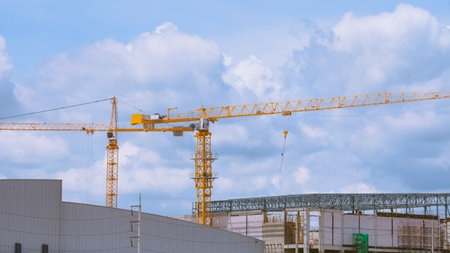 Factory buildings structure with tower cranes in construction site area against cloudy sky backgroundの写真素材