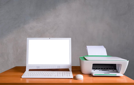 White computer with wireless keyboard and printer on wooden desk in front of gray concrete loft wall...