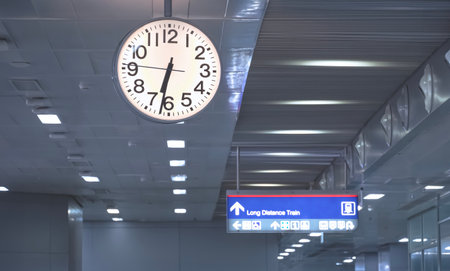 Selective focus at hanging clock with information signs label on ceiling inside of modern train station building, low angle view with copy spaceの写真素材
