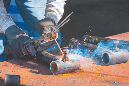 Close up of welder hand using arc welding machine to welding nut and bolts on galvanized steel pipe for apply to metal joint in construction site areaの写真素材