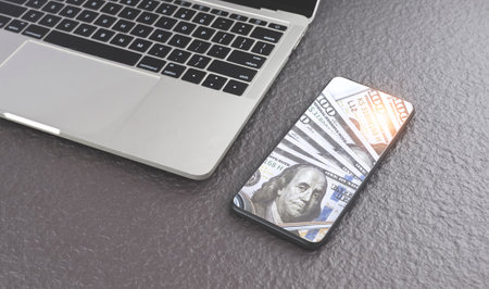 Dollar banknotes image inside of smartphone screen with laptop on gray stone tabletop, business and financial online design conceptの写真素材