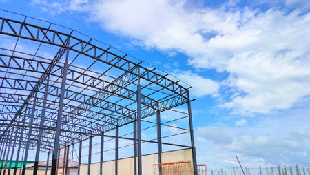 Metal roof beam and columns of warehouse building structure in construction site area against clouds on blue sky background, Low angle and perspective side viewの写真素材