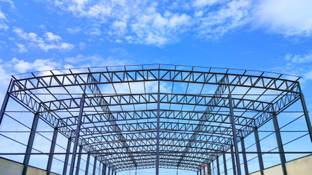 Metal roof beam and columns of new warehouse building structure in construction site area against blue sky background, Low angle and symmetric viewの写真素材