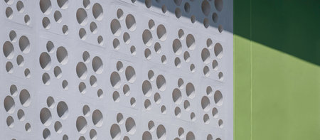Sunlight and shadow on circular pattern of white ventilation blocks and green concrete wall of modern house in panoramic viewの写真素材