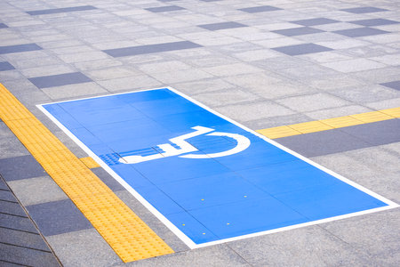Accessible wheelchair sign with yellow tactile paving lines on marble pavement surface in public areaの写真素材