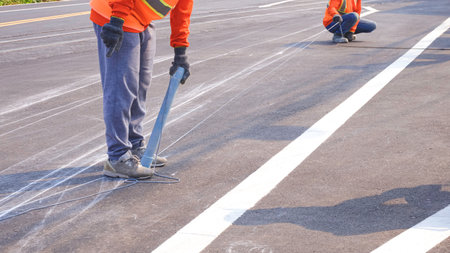 Cropped image of 2 road workers marking line for painting traffic color lines on asphalt road with railway track crossing on street surfaceの写真素材