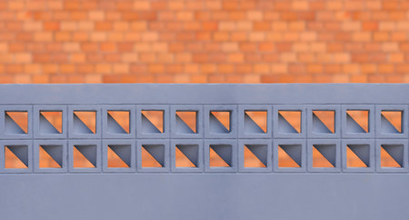 Gray painted concrete fence wall with geometric pattern of ventilation blocks in front of blurred brick house wall backgroundの写真素材