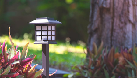 Little black steel ground lantern in vintage style on walkway with ornamental plant and blurred background of the bole of tree in home gardening areaの写真素材