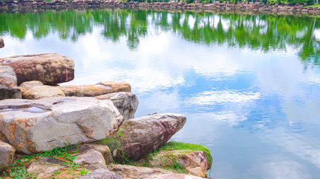 Beautiful landscape view of lake and sky reflection on water surface with rocks around the large pond in public park areaの写真素材