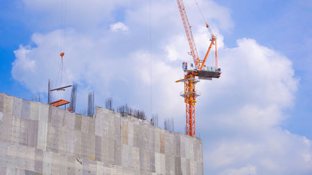 Tower crane are working on top of high building structure against white clouds on blue sky backgroundの写真素材