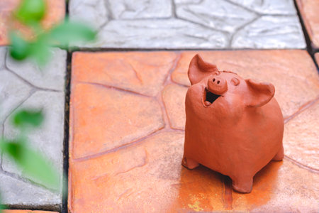 Ornamental terracotta garden doll in the shape of little adorable pig smiling happily on stone tile pavement floor in home gardenの写真素材