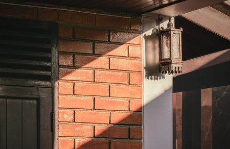 Sunlight and shadow on surface of the old retro wall lamp on brick and teak wood wall of vintage detached houseの写真素材