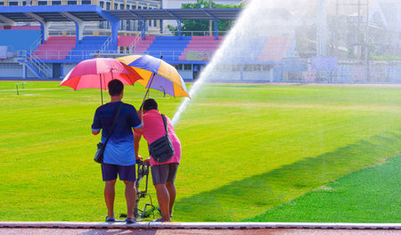 Two workers using big gun high pressure sprinkler to watering grass field in large soccer stadiumの写真素材