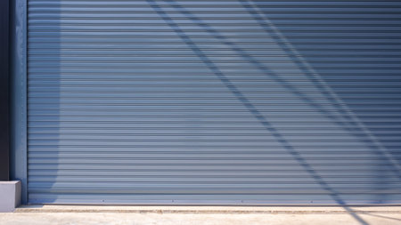 Automatic gray roller shutter entrance door of industrial warehouse building with sunlight and...