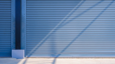 Automatic gray roller shutter entrance doors of large industrial warehouse building with light and shadow on concrete floor surfaceの写真素材