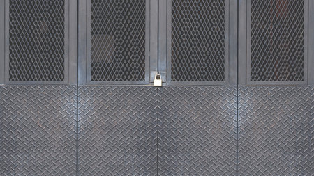 Black metal foldable entrance door background made from carbon steel diamond plate with grid wire mesh in industrial modern loft style, front view with copy spaceの写真素材