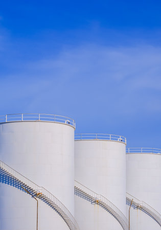 Three white storage fuel tanks in petroleum industry area against blue sky background in vertical frameの写真素材