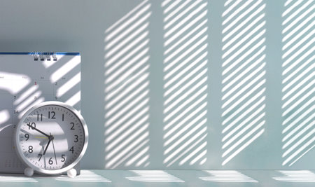 White round table clock and desk calendar on tabletop with morning sunlight and shadow on surface, panoramic view with copy space, Minimal workspace backgroundの写真素材