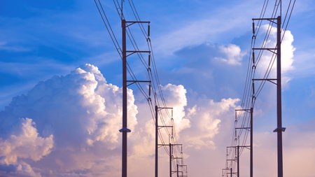 Silhouette two rows of electric poles and cable lines against big white cloudy on blue sky...