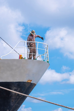 Asian blue collar worker is painting balustrade on the bow of the old oil tanker ship at shipyard during renovation work, full length view and vertical frameの写真素材