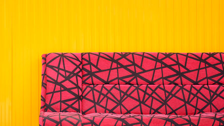 Red fabric sofa with black abstract pattern in modern style in front of yellow aluminium wall backgroundの写真素材