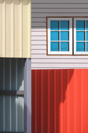 Geometric colorful lines pattern background in street minimal style, Focus at window of wooden house with blurred storehouse and steel fence on foreground in vertical frameの写真素材