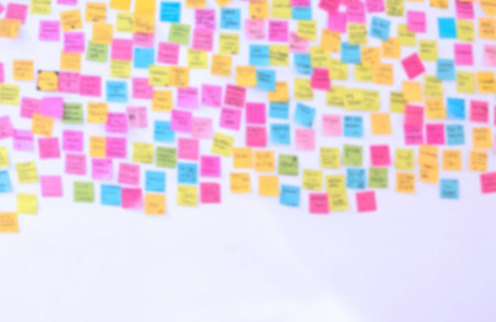 Blurred background of many colorful sticky notes with lots of text on white wall for backdrop designの写真素材