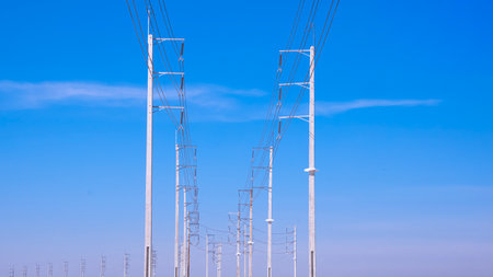 Two rows of electric poles with cable lines on curve country road against blue sky background, low...