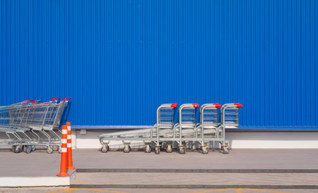 Row of shopping carts on pavement floor in front of blue aluminum corrugated metal wall of modern hypermarketの写真素材