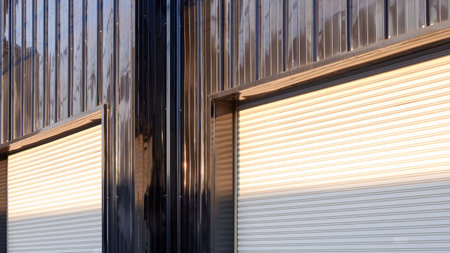 Two automatic white roller shutter entrance doors on black corrugated metal wall of modern building...
