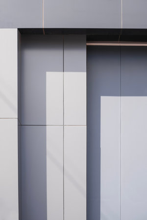 Gray aluminium composite tile wall decoration in steps pattern outside of modern building with sunlight and shadow on surface, Exterior geometric architecture vertical background in minimal styleの写真素材