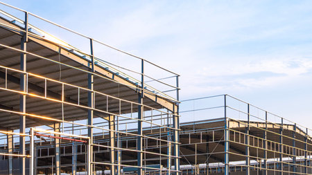 Metal structure of 2 factory warehouse industry buildings in construction site against pale blue sky...