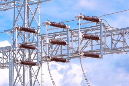 Insulators on high voltage electric pylon structure in power distribution substation against blue sky backgroundの写真素材