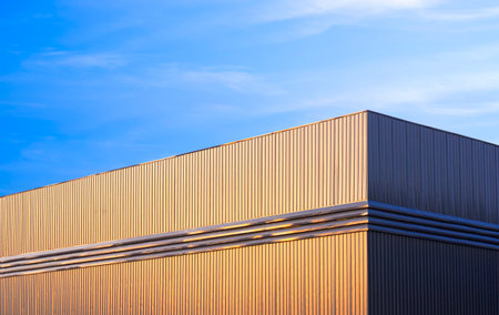 Warehouse factory building with golden sunlight on gray aluminium corrugated steel wall against blue...