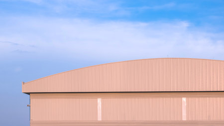 Large warehouse factory industrial building with dome roof and louver ventilation on aluminium corrugated metal wall against blue sky background, front view with copy spaceの写真素材
