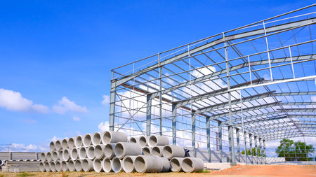 Metal structure of warehouse industrial factory building with concrete drainage pipes stacked on the...