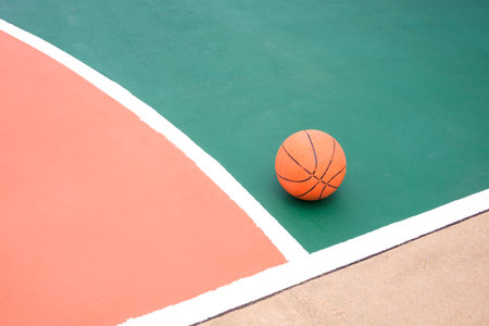 Basketball on colorful green and orange with white outline of outdoor basketball courtの写真素材