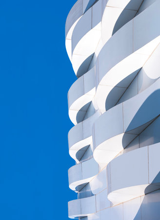 Building exterior modern architecture design, 3d dimension curve pattern of geometric white aluminium composite tile wall decoration against blue sky vertical backgroundの写真素材