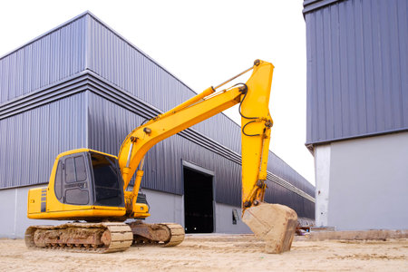 Excavator on the ground in front of industrial warehouse factory buildings structure in construction...