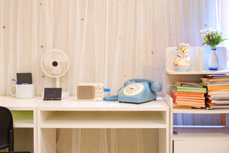 Vintage dial telephone and speaker with personal accessories on wooden desk with bookshelf in modern white living room, front view with copy spaceの写真素材