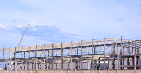 Metal structure of large factory industrial building framework with crane truck are working in construction site against blue sky background, Side view with copy spaceの写真素材